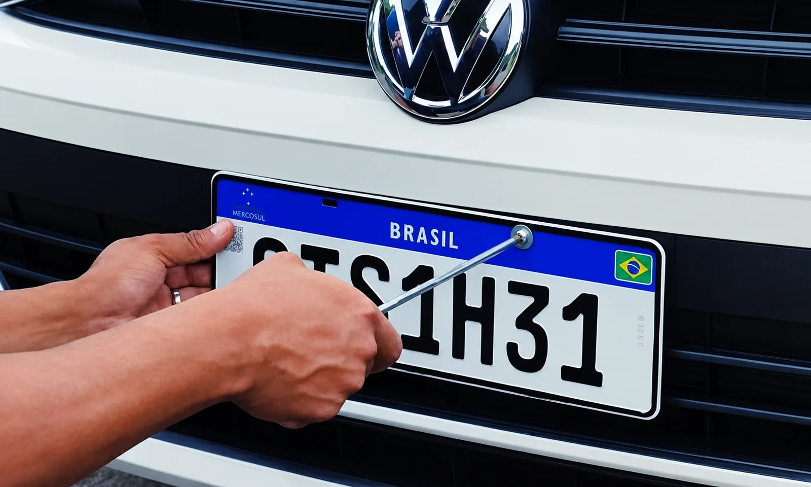 Placa Mercosul sendo parafusada na dianteira de um veículo durante o emplacamento